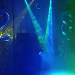 Scena oświetlona reflektorami w kolorach niebieskim i zielonym, z balonami i dekoracjami w tle.