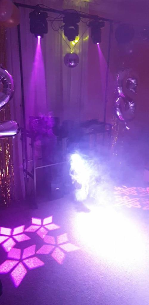 Scena oświetlona reflektorami z efektami świetlnymi w kształcie płatków śniegu na podłodze, dekoracje balonowe i błyszczące frędzle w tle.