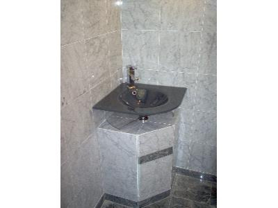 Narożna umywalka z czarnego kamienia na marmurowej podstawie w łazience wyłożonej marmurowymi płytkami, bateria chromowana.