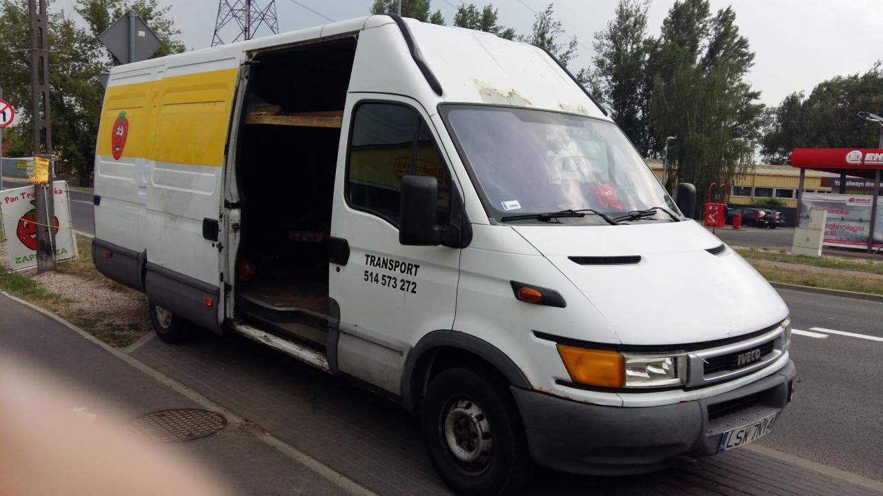 Biały samochód dostawczy marki Iveco z otwartymi drzwiami bocznymi, zaparkowany na ulicy, z napisem 'TRANSPORT 514 573 272' i grafiką truskawki na żółtym tle.