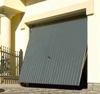 Częściowo otwarta, szara brama garażowa segmentowa z pionowymi przetłoczeniami, widoczna z niskiej perspektywy, z fragmentem ogrodzenia i elewacji budynku w tle.