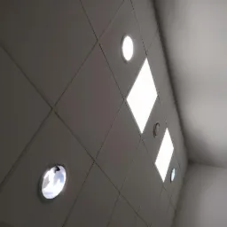 Rzut z dołu na sufit podwieszany z kwadratowymi panelami i okrągłymi lampami LED, oświetlenie włączone, widoczny fragment ściany.