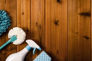 Ściereczka z mikrofibry, miotełka do kurzu, gąbka i butelka ze spryskiwaczem na tle drewnianych paneli.