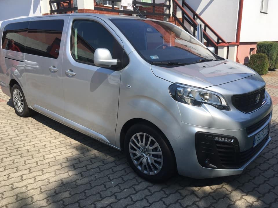 Srebrny van Peugeot Expert Kombi na brukowanym podjeździe przed domem z czerwonymi schodami.