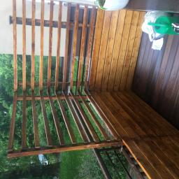 Lessandra sp. Z o.o. - Świeżo pomalowana drewniana konstrukcja altany z widocznymi smugami mokrej farby i odbiciami, z zielonymi drzewami w tle.