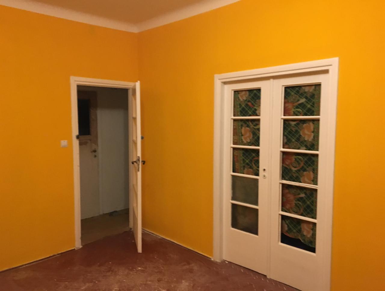 Pokój z pomalowanymi na jaskrawy żółty kolor ścianami, białe drzwi wewnętrzne z szybami z wzorzystą folią dekoracyjną, otwarte drzwi do sąsiedniego pomieszczenia.