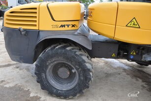 Żółta koparka kołowa Mecalac 12 MTX z widocznym bieżnikiem opony i oznaczeniami modelu, stojąca na szarym podłożu.
