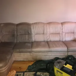 Beżowa narożna kanapa z widoczną różnicą w czystości tapicerki, połowa wyczyszczona, obok żółty odkurzacz piorący Karcher Z8 i folia ochronna.