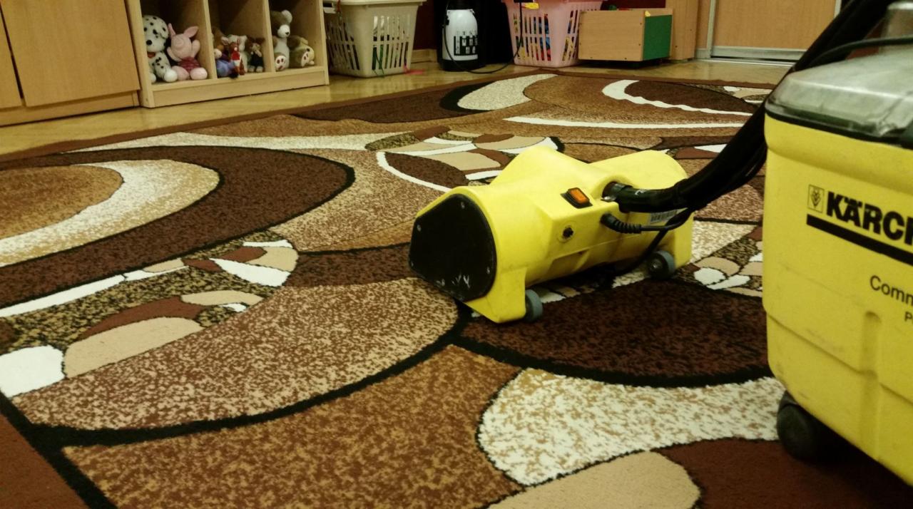 Żółty odkurzacz piorący Karcher na brązowym dywanie we wzory w pokoju dziecięcym z półkami pełnymi zabawek w tle.