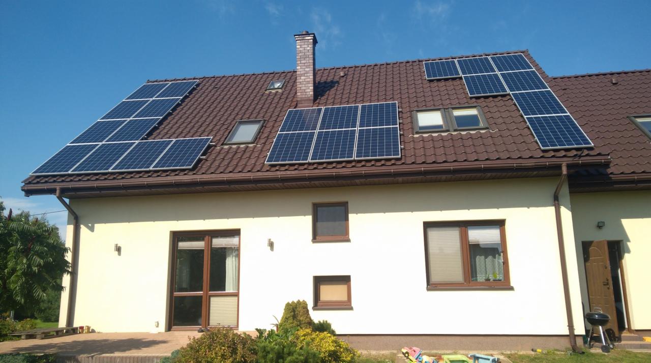 Dom jednorodzinny z brązowym dachem, na którym zamontowane są panele słoneczne w kilku sekcjach, widoczne okna dachowe i komin z cegły.