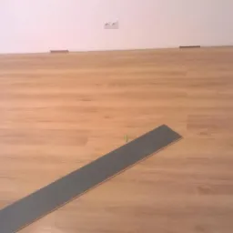 Układanie paneli podłogowych: widok na fragment ułożonej podłogi z paneli imitujących drewno, pojedynczy panel leżący na podłodze, widoczne dystanse przy ścianie, gniazdko elektryczne na ścianie...