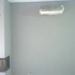 Szara ściana po tynkowaniu maszynowym z zaklejonym otworem i kominkiem w rogu pokoju.