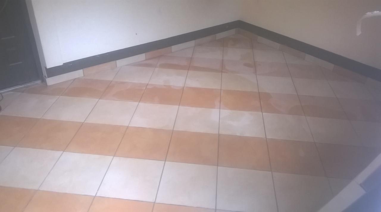 Ułożona podłoga z płytek w biało-pomarańczowe pasy, widoczna listwa przypodłogowa i fragment drzwi.