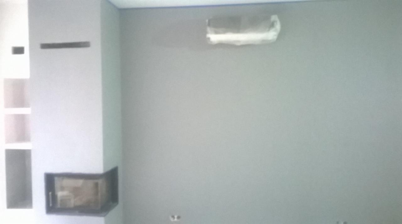 Szara ściana po tynkowaniu maszynowym z zaklejonym otworem i kominkiem w rogu pokoju.