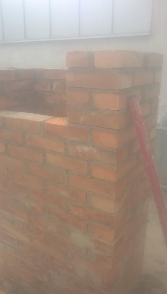 Fragment murowanej ściany z czerwonej cegły, widoczny pionowy element konstrukcyjny i fragment ściany w tle, całość w delikatnej mgle.