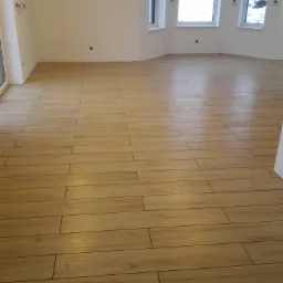 Ułożona podłoga z płytek imitujących drewno w jasnym, pustym pokoju z trzema oknami z widokiem na zaśnieżony ogród.