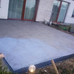 MAZUR usługi remontowo-budowlane Andrzej Walczak - Wylewka betonowa na tarasie w trakcie schnięcia, widoczne narzędzia i materiały przygotowane do dalszych prac wykończeniowych, w tle elewacja domu.