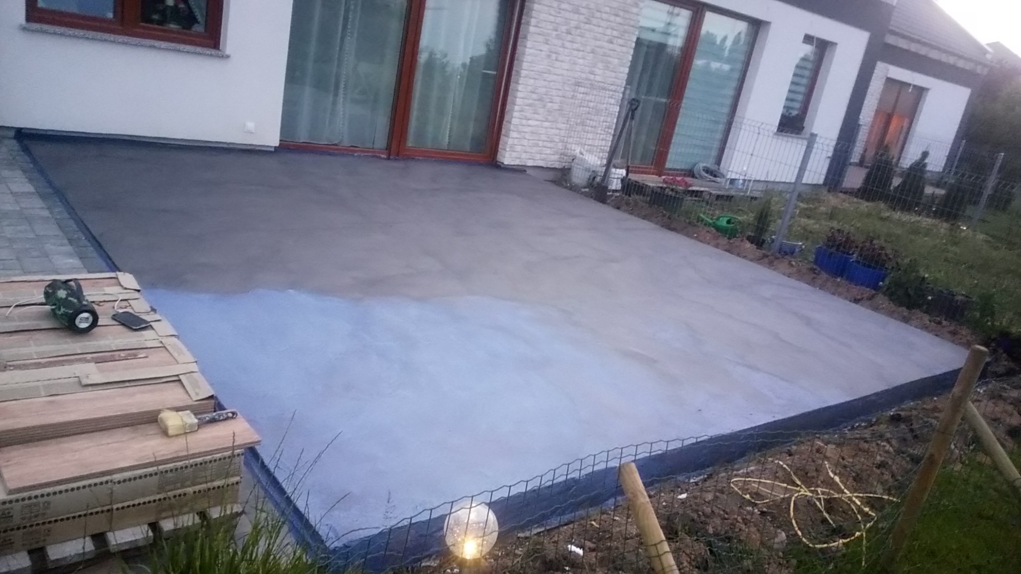 Wylewka betonowa na tarasie w trakcie schnięcia, widoczne narzędzia i materiały przygotowane do dalszych prac wykończeniowych, w tle elewacja domu.