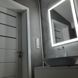 BEST HOME MARIUSZ MIKOŁAJCZYK - Nowoczesna łazienka z szarą płytką, umywalką nablatową i podświetlanym lustrem LED, widok na drzwi z poziomymi frezowaniami i włącznik światła