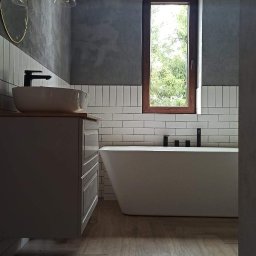 BEST HOME MARIUSZ MIKOŁAJCZYK - Nowoczesna łazienka z wolnostojącą wanną, umywalką nablatową i drewnopodobną podłogą, wykończona białymi, pionowymi płytkami oraz szarą, betonową ścianą.