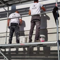 BEST HOME MARIUSZ MIKOŁAJCZYK - Dwóch pracowników na rusztowaniu wyrównuje ścianę zewnętrzną za pomocą szpachli, widoczne wiadra z masą szpachlową Ceresit, ubrania robocze z zabrudzeniami.