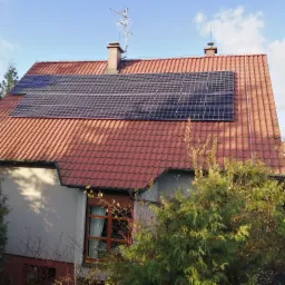 Panele słoneczne na czerwonym dachu domu jednorodzinnego, widoczne z poziomu gruntu, antena telewizyjna na kominie