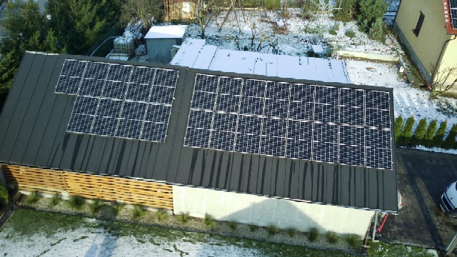 Instalacja paneli słonecznych na dachu budynku z drewnianą elewacją, częściowo pokrytym śniegiem, widok z góry.