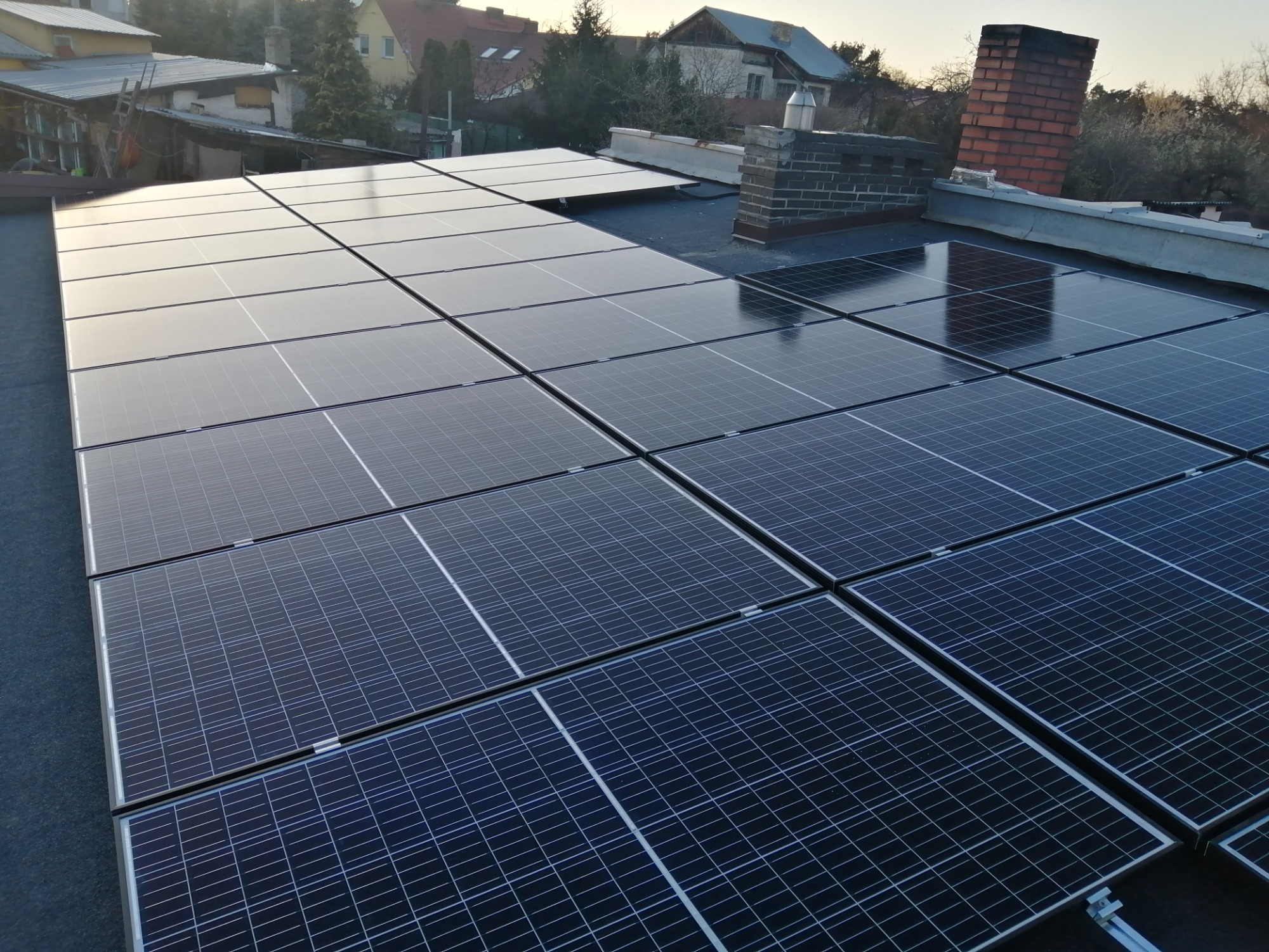 Instalacja paneli słonecznych na dachu domu jednorodzinnego, widok z góry, komin z czerwonej cegły w tle.