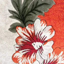 Fragment dywanu z wzorem kwiatowym w odcieniach bieli, czerwieni i szarości, prezentujący detale włókien i strukturę materiału.