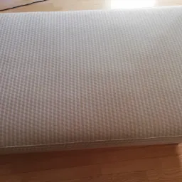 Tapicerowane siedzisko ławki lub kanapy z geometrycznym wzorem 3D w odcieniach beżu, widoczne na tle drewnianej podłogi.