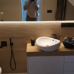 Nowoczesna łazienka w odcieniach beżu z podświetlanym lustrem, umywalką nablatową w kształcie łzy i czarną armaturą, widoczne detale dekoracyjne i toaleta z bidetką.