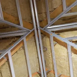 Szkielet sufitu podwieszanego z profili metalowych, wypełniony wełną mineralną, widoczne drewniane elementy konstrukcyjne dachu.