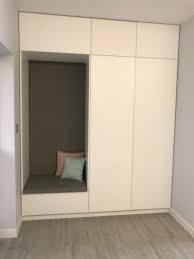 Biała zabudowa wnęki z siedziskiem i poduszkami, po prawej szafa z frontami bez uchwytów, drewniana podłoga.