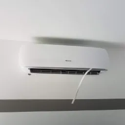 Biała jednostka wewnętrzna klimatyzatora marki Hisense zamontowana na ścianie z szarym pasem dekoracyjnym, widoczny przewód instalacyjny.