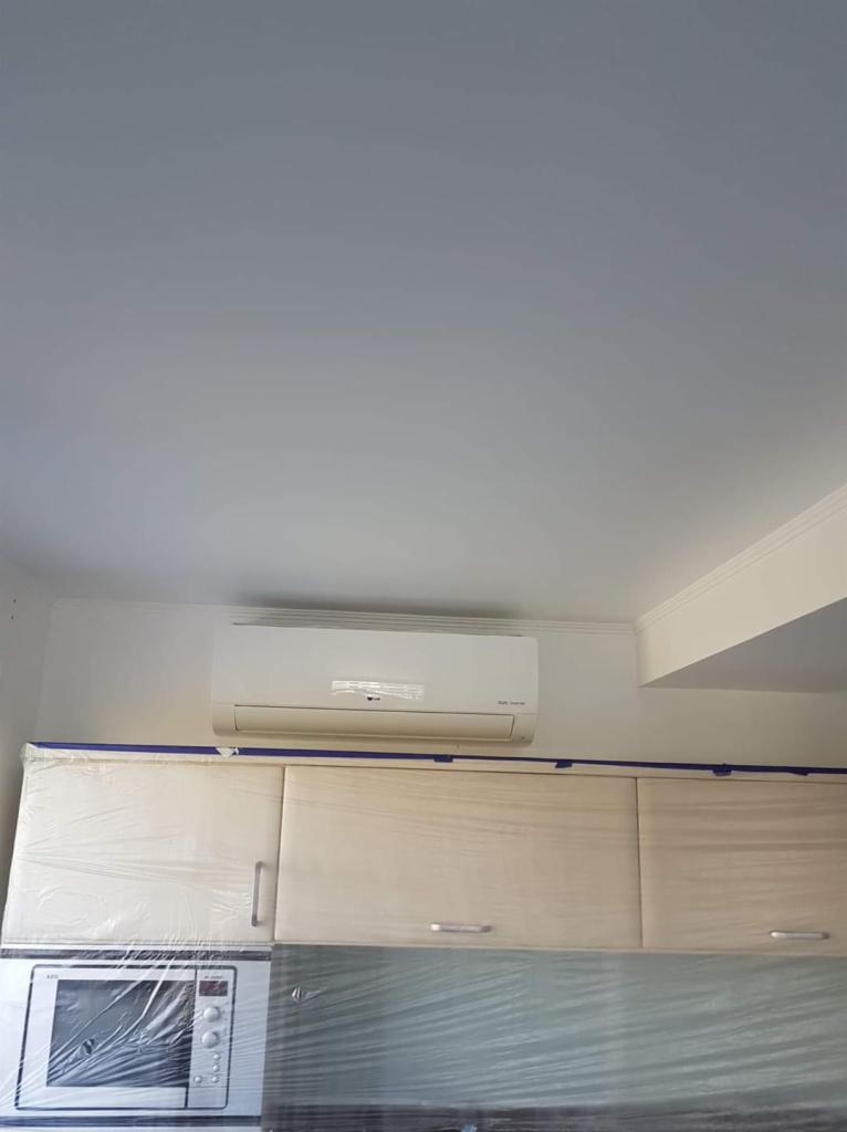 Biała jednostka wewnętrzna klimatyzatora marki LG zamontowana na ścianie nad szafkami kuchennymi, zabezpieczonymi folią i taśmą malarską.