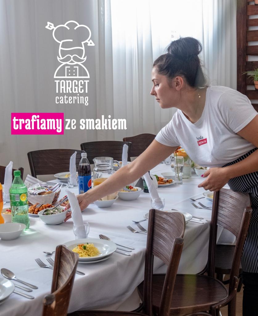 Kelnerka w fartuchu ustawia białe serwetki na długim stole z białym obrusem, nakrytym do posiłku, z napojami i potrawami.