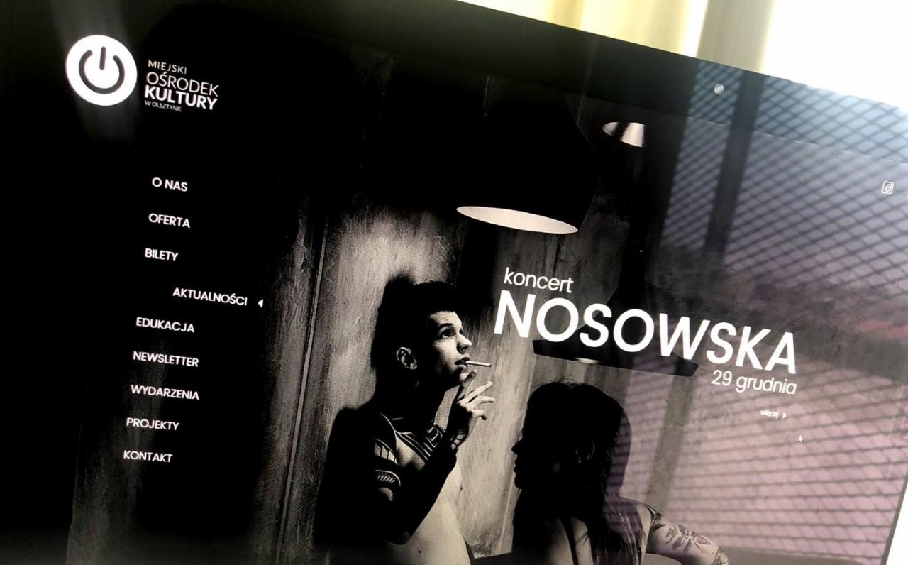 Ekran monitora prezentujący czarno-białą stronę internetową Miejskiego Ośrodka Kultury w Olsztynie, z informacją o koncercie Nosowskiej 29 grudnia, widoczne menu po lewej stronie.