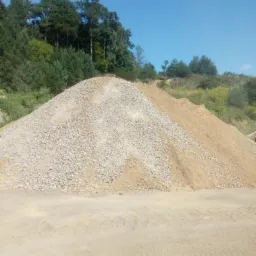 Kopalnia piasku i żwiru: duży pryzmatyczny kopiec żwiru i piasku na tle drzew i błękitnego nieba.