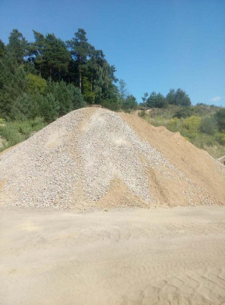 Kopalnia piasku i żwiru: duży pryzmatyczny kopiec żwiru i piasku na tle drzew i błękitnego nieba.