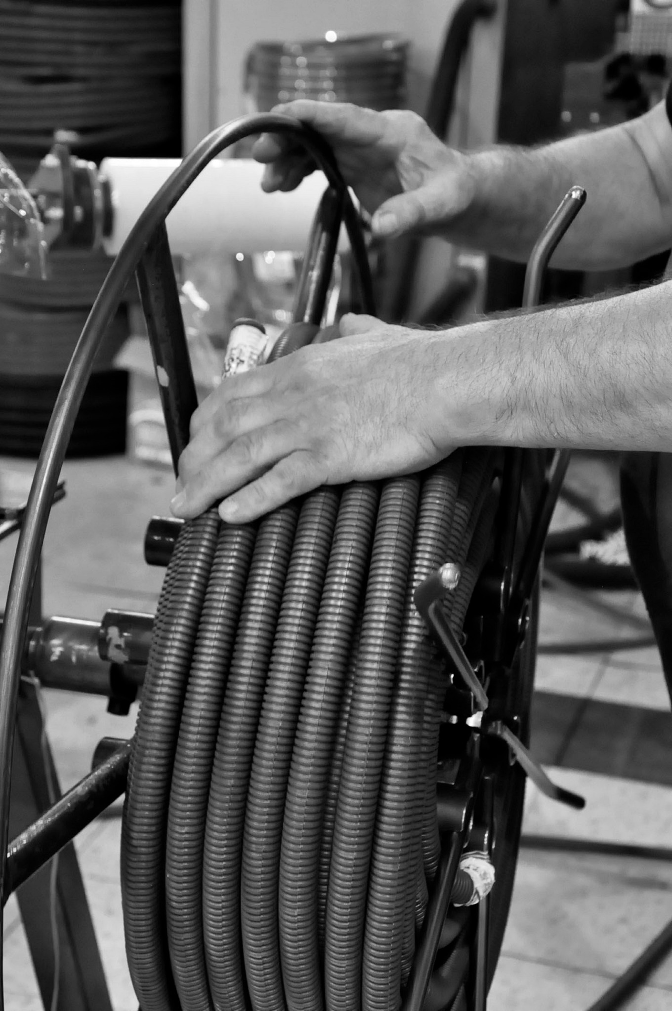 Czarno-białe zdjęcie zwiniętego kabla w metalowej obudowie, trzymanego przez dłonie mężczyzny, prawdopodobnie podczas rozwijania lub zwijania.