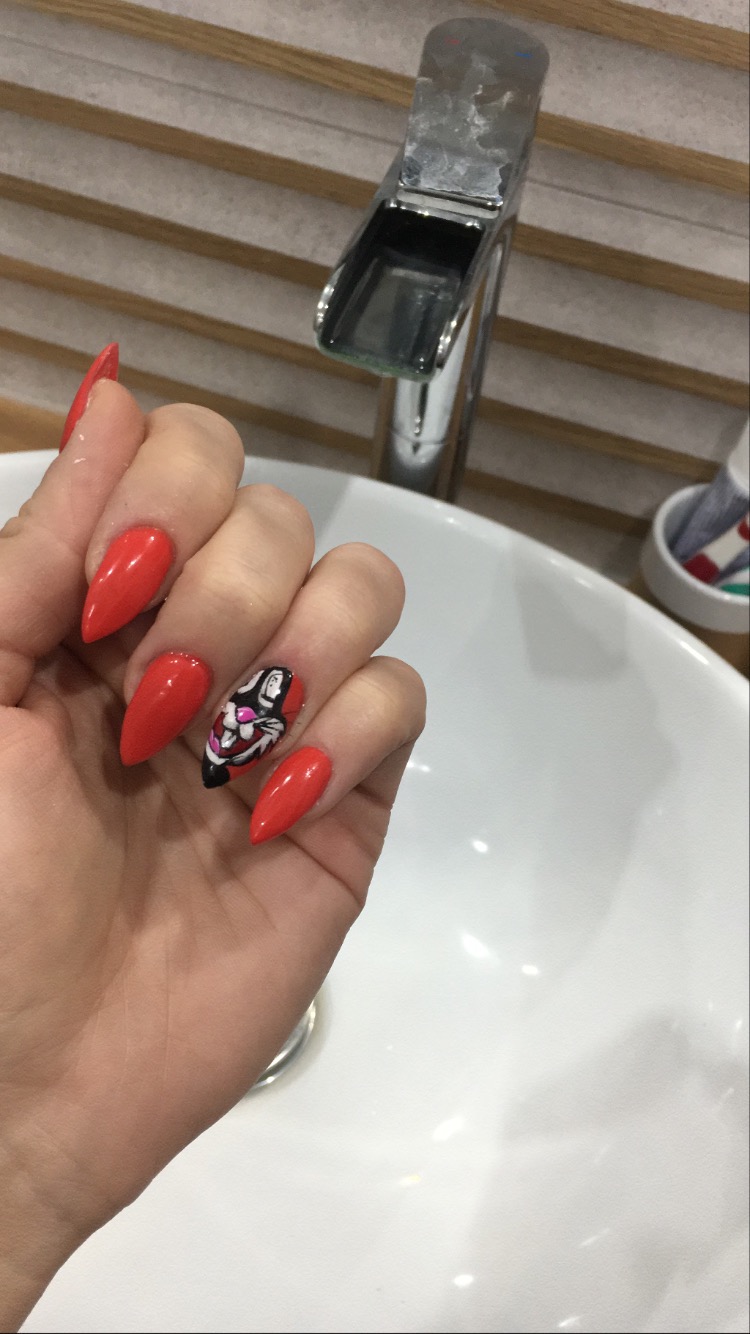 Dłoń z czerwonymi, ostrymi paznokciami; jeden paznokieć ozdobiony czarno-białym rysunkiem twarzy kobiety z czerwonymi ustami, na tle umywalki i baterii.