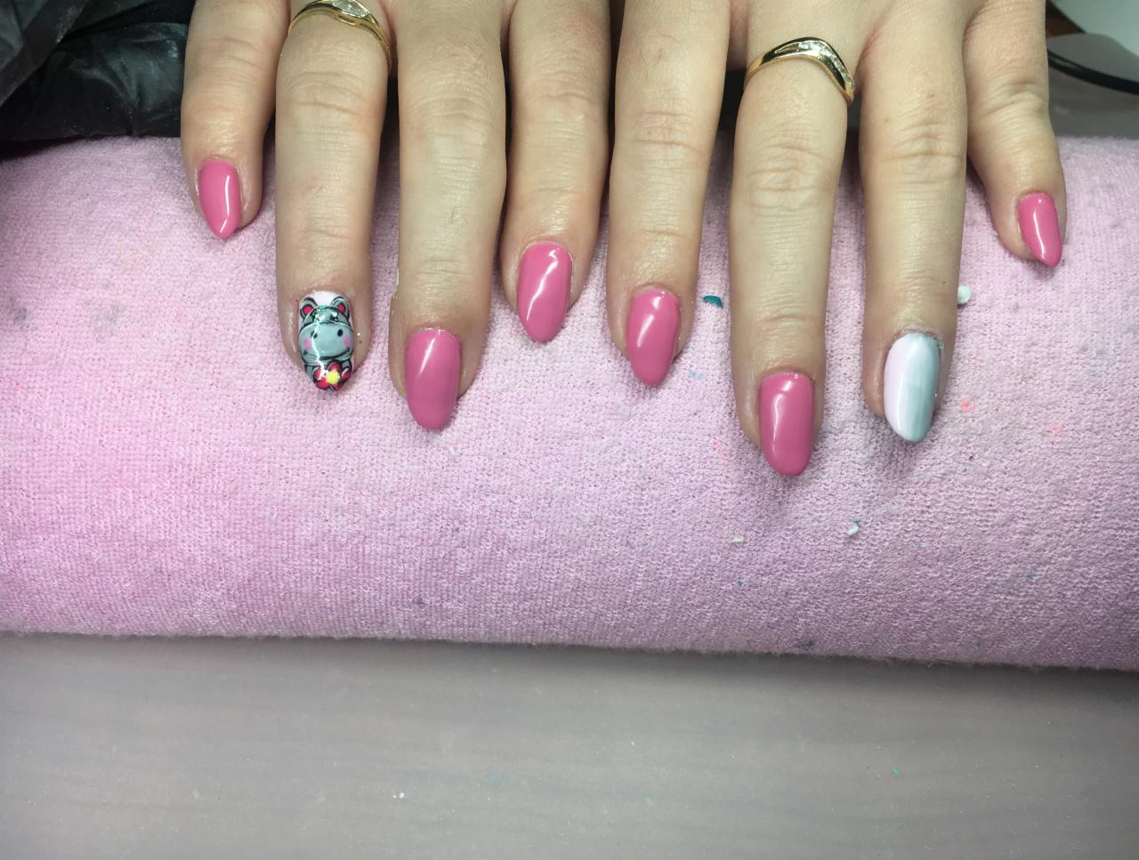 Ręka z pomalowanymi paznokciami w odcieniach różu, jeden paznokieć z motywem zwierzęcym, a drugi w kolorze ombre, na różowym ręczniku.