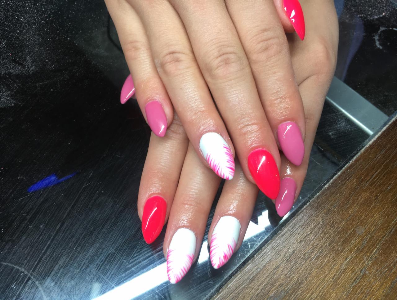 Dłonie z pomalowanymi paznokciami w odcieniach różu i czerwieni; dwa paznokcie białe z różowymi promienistymi zdobieniami.