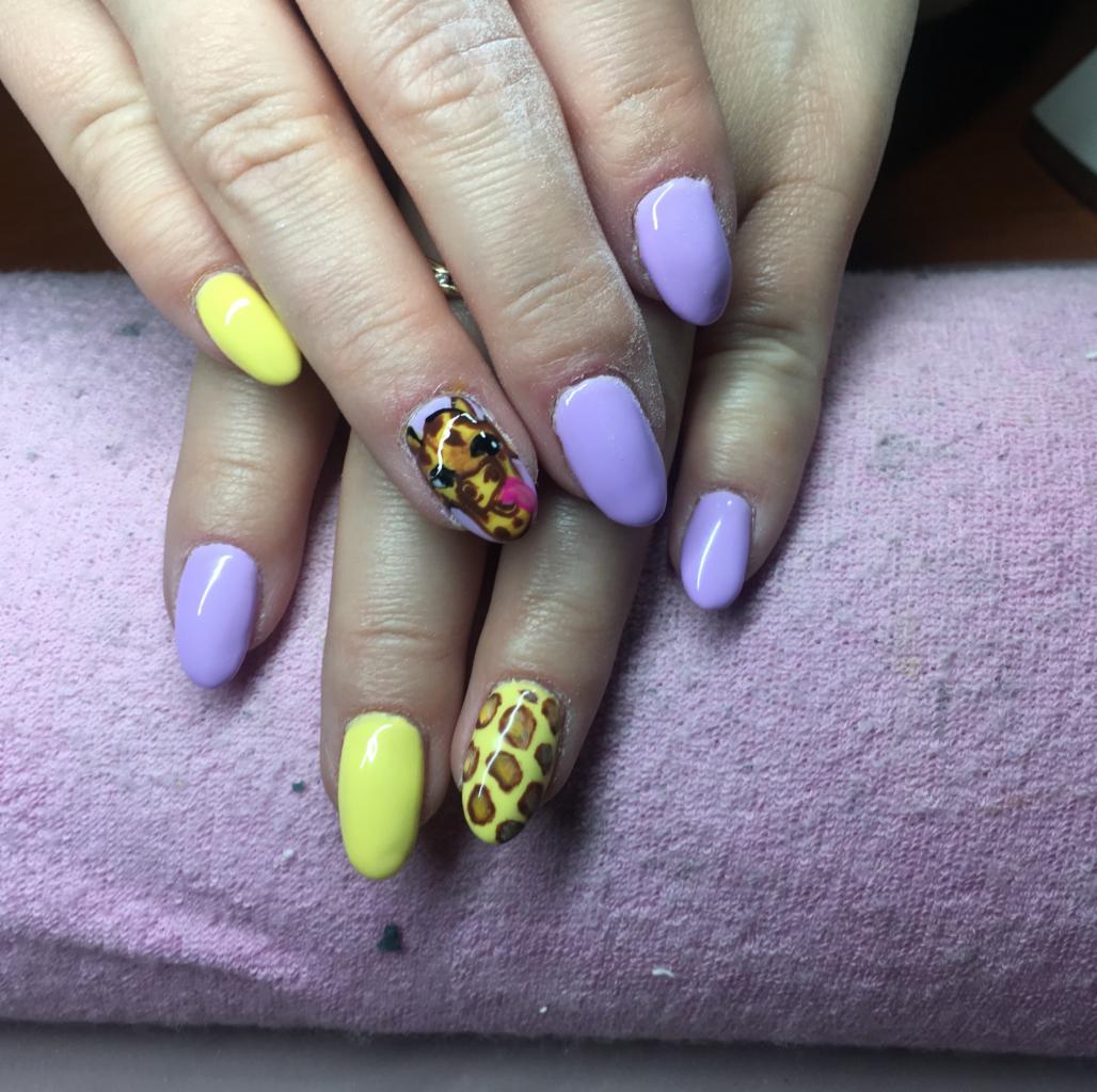 Dłonie z pomalowanymi paznokciami: fioletowe, żółte oraz z motywem żyrafy i zwierzęcymi cętkami na różowym tle.