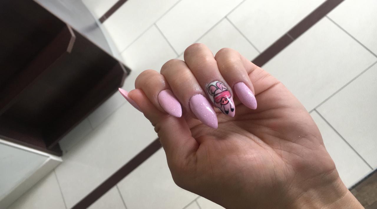 Ręka z delikatnym, różowym manicure hybrydowym, jeden paznokieć ozdobiony rysunkiem świnki w okularach przeciwsłonecznych.