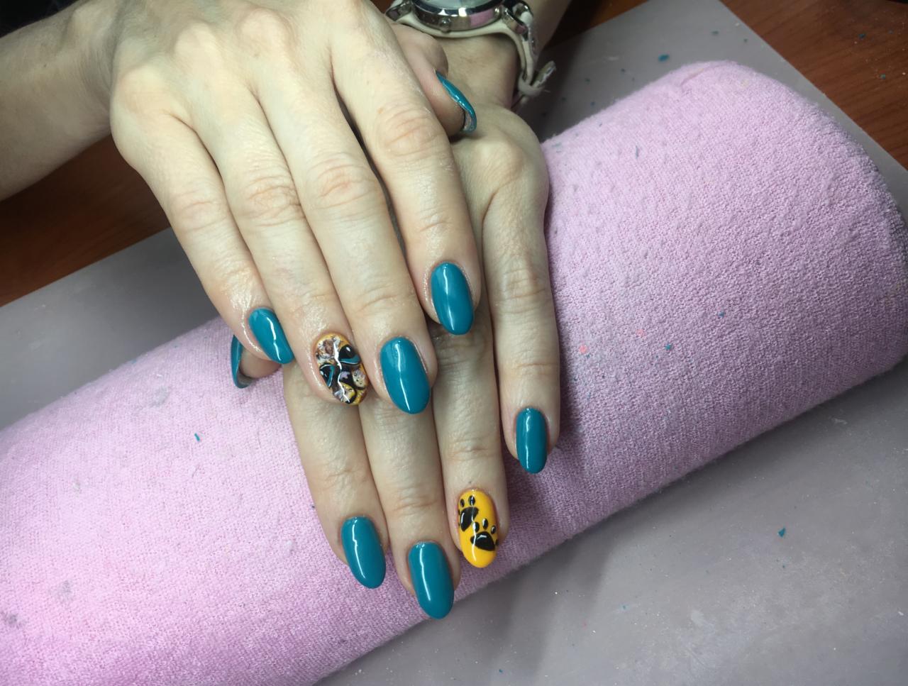 Turkusowe paznokcie z wzorami (motyl i łapki) wykonane we Wrocławiu na różowym podkładzie, widoczne dłonie i nadgarstek z zegarkiem.