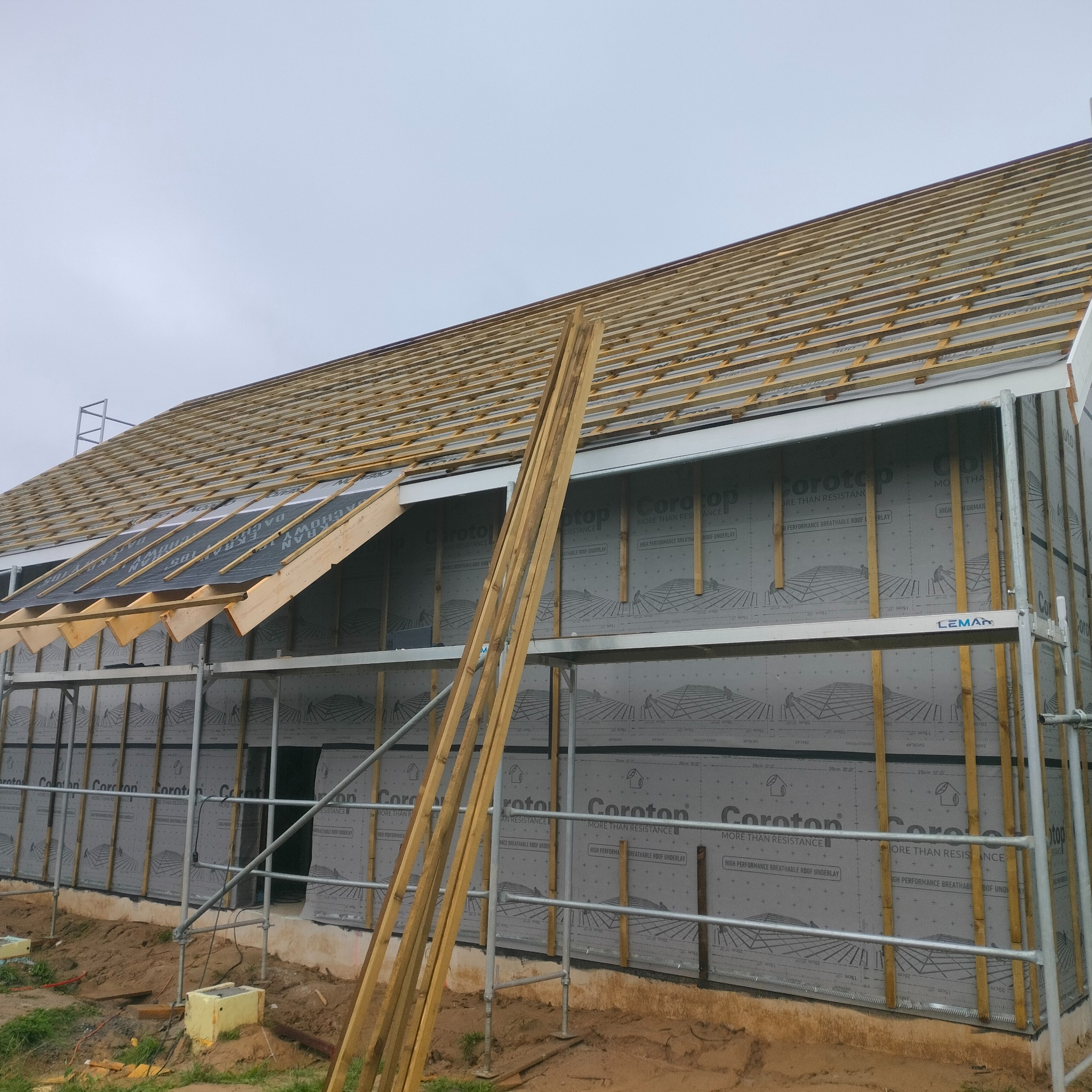 Konstrukcja szkieletowa domu w trakcie budowy: widoczne ściany z membraną Corotop, rusztowanie i częściowo ułożone łaty dachowe pod blachodachówkę.