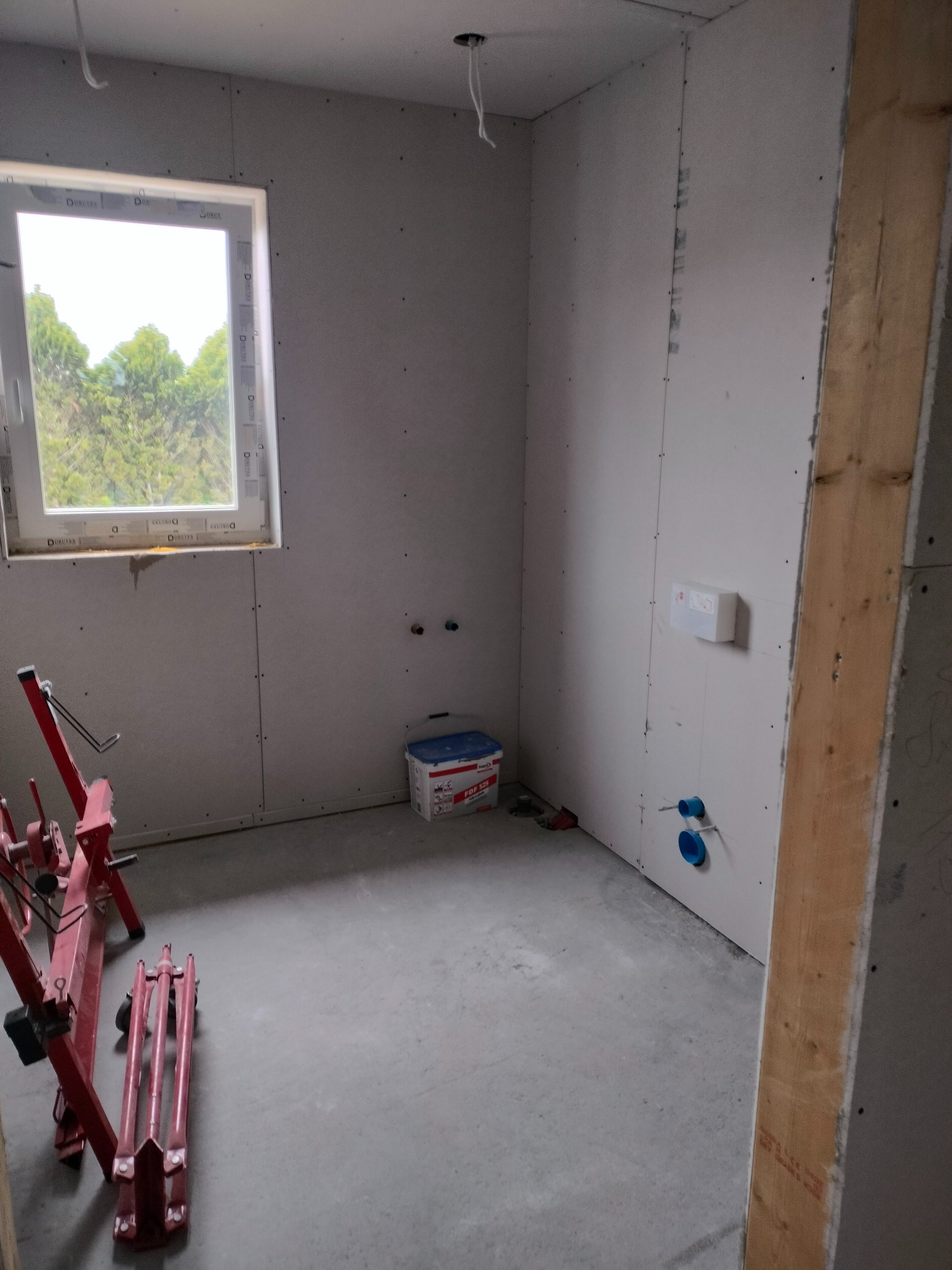 Wnętrze domu szkieletowego w trakcie wykańczania płytami gipsowo-kartonowymi, widoczne narzędzia i puszka z masą szpachlową.