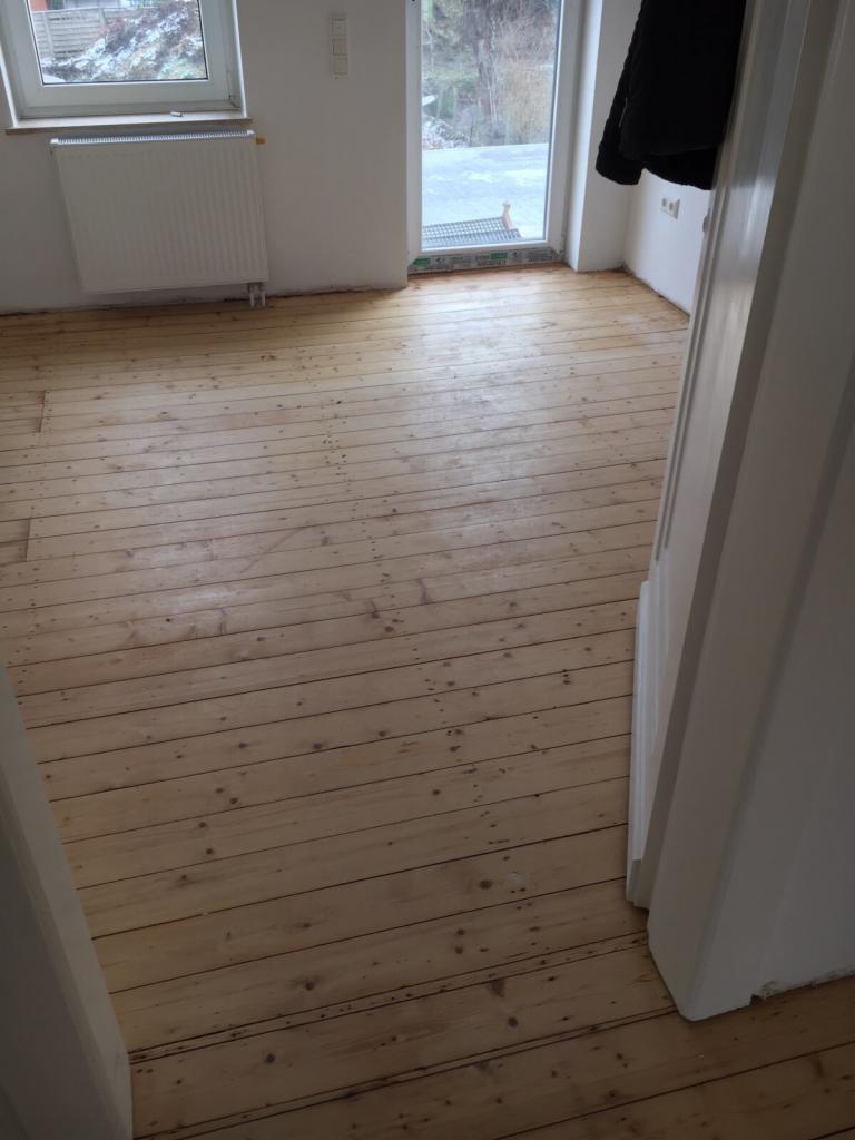 Jasna, odnowiona podłoga z desek w pokoju z grzejnikiem i oknem, widok z perspektywy progu drzwi.