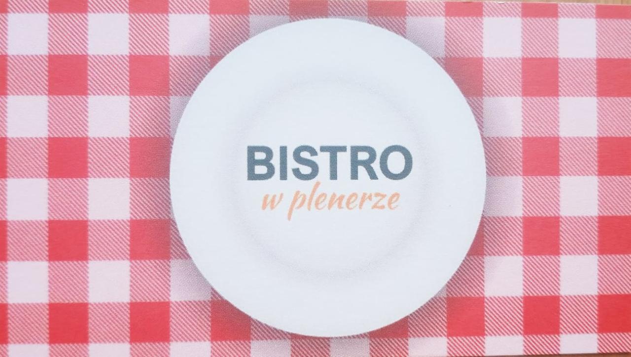 Logo Bistro w plenerze na białym talerzu, umieszczone na czerwono-białym obrusie w kratę.